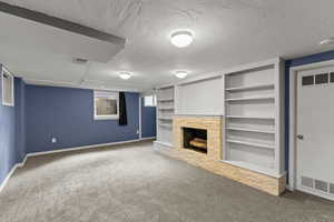 Unfurnished living room featuring a stone fireplace, carpet flooring, a textured ceiling, and built in shelves