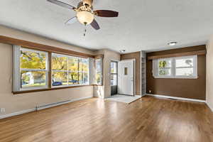 Unfurnished living room with light wood-style flooring, baseboard heating, ceiling fan, and a textured ceiling