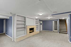 Unfurnished living room featuring light colored carpet, a textured ceiling, a fireplace with raised hearth, stairs, and built in features