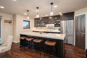 Bar featuring appliances with stainless steel finishes, decorative backsplash, dark brown cabinets, light stone counters, and dark wood-type flooring