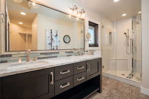 Full bath featuring recessed lighting, double vanity, a stall shower, decorative backsplash, and light wood-style floors