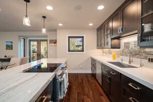 Kitchen with stainless steel appliances, hanging light fixtures, dark wood-type flooring, glass insert cabinets, and recessed lighting
