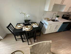Kitchen featuring white cabinetry, black dishwasher, light wood finished floors, and light stone countertops
