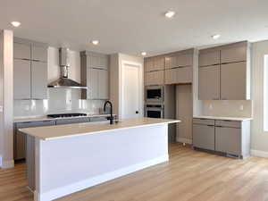 Kitchen featuring gray cabinets, wall chimney range hood, modern cabinets, appliances with stainless steel finishes, and a textured ceiling