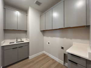 Laundry area featuring a textured ceiling, light wood-style floors, washer hookup, cabinet space, and electric dryer hookup