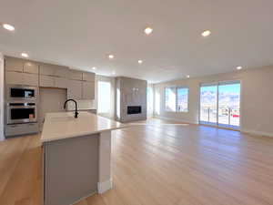 Kitchen with gray cabinetry, modern cabinets, a center island with sink, open floor plan, and appliances with stainless steel finishes