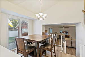 Dining space with wood finished floors, a chandelier, ceiling fan, and high vaulted ceiling