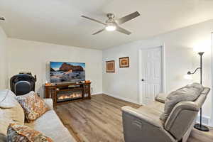 Living room with wood finished floors, a glass covered fireplace, and ceiling fan