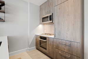Kitchen featuring tasteful backsplash, modern cabinets, stainless steel appliances, light countertops, and light wood finished floors