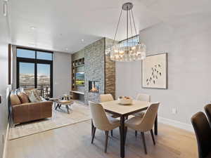 Dining area with light wood finished floors, a stone fireplace, built in features, and a chandelier