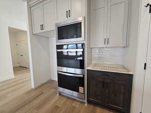 Kitchen with stainless steel appliances, tasteful backsplash, light wood-style floors, and dark brown cabinets