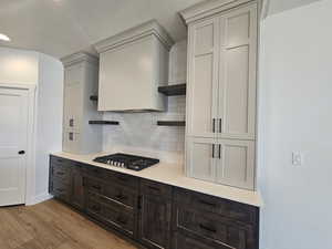 Kitchen featuring open shelves, backsplash, dark brown cabinetry, light wood-style flooring, and stainless steel gas stovetop