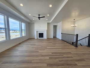 Unfurnished living room featuring a raised ceiling, recessed lighting, a ceiling fan, a fireplace, and light wood finished floors