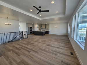 Unfurnished living room featuring a chandelier, healthy amount of natural light, a raised ceiling, and recessed lighting