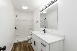 Full bath featuring dark wood finished floors, vanity, and a stall shower