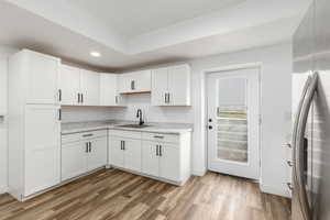 Kitchen with freestanding refrigerator, white cabinetry, light countertops, tasteful backsplash, and light wood-type flooring