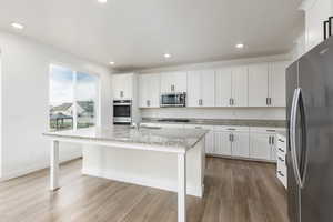 Kitchen featuring appliances with stainless steel finishes, light stone countertops, a center island with sink, light wood-style floors, and white cabinetry