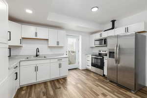 Kitchen featuring stainless steel appliances, white cabinetry, light wood-style flooring, backsplash, and recessed lighting