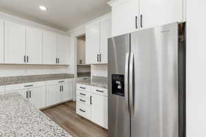 Kitchen with stainless steel fridge, light wood-style floors, white cabinets, light stone counters, and recessed lighting