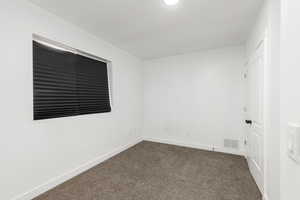 Unfurnished room featuring dark colored carpet and baseboards