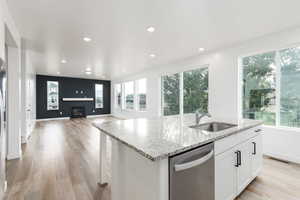 Kitchen with a center island with sink, dishwasher, light stone countertops, white cabinets, and a glass covered fireplace