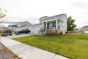 View of front of home featuring concrete driveway, a front lawn, a porch, stone siding, and an attached garage