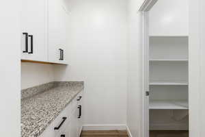 Bar area featuring white cabinets, light stone countertops, and light wood-type flooring