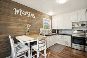 Kitchen featuring stainless steel range with electric stovetop, dark countertops, white cabinetry, dark wood-style floors, and wood walls