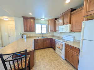 Kitchen featuring white appliances, light countertops, a peninsula, recessed lighting, and brown cabinetry