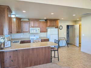 Kitchen featuring brown cabinets, white appliances, recessed lighting, a peninsula, and a kitchen breakfast bar