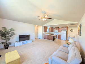 Living room with lofted ceiling, ceiling fan, light carpet, and a textured ceiling