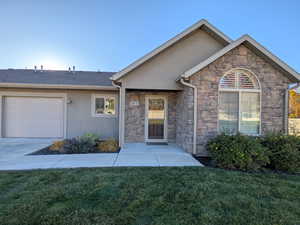 View of front of property with a front lawn, an attached garage, stone siding, and stucco siding
