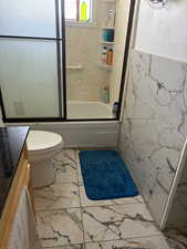 Bathroom with enclosed tub / shower combo, tile walls, vanity, and light marble finish flooring