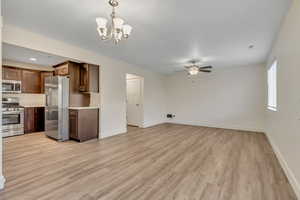 Unfurnished living room with light wood-style flooring, a chandelier, and ceiling fan