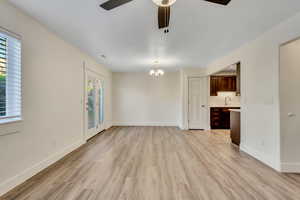 Unfurnished living room featuring light wood-type flooring, a chandelier, and a ceiling fan