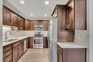Kitchen with stainless steel appliances, recessed lighting, light stone countertops, light wood-style flooring, and dark brown cabinets