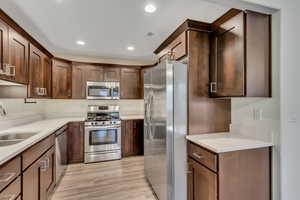Kitchen with appliances with stainless steel finishes, recessed lighting, light stone countertops, light wood-style floors, and dark brown cabinets