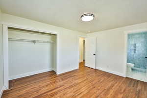 Unfurnished bedroom with wood finished floors, a closet, a textured ceiling, and ensuite bath