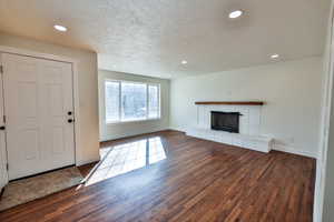 Unfurnished living room with dark wood-type flooring, a textured ceiling, recessed lighting, and a fireplace