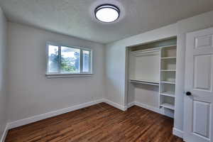 Unfurnished bedroom featuring a textured ceiling, dark wood finished floors, and a closet