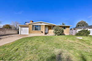 Single story home featuring brick siding, a chimney, driveway, and an attached garage