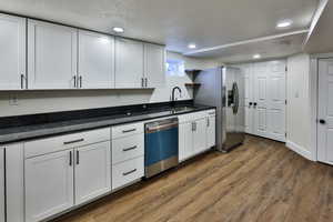 Kitchen with white cabinets, a textured ceiling, dark wood-style floors, dishwasher, and recessed lighting