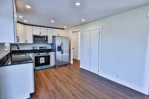 Kitchen featuring appliances with stainless steel finishes, white cabinetry, dark stone counters, dark wood-type flooring, and recessed lighting