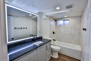 Full bath featuring a textured ceiling, vanity, dark wood-type flooring,  shower combination, and recessed lighting