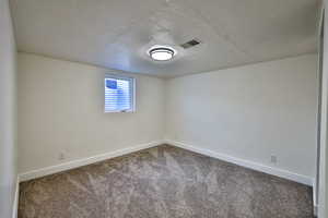 Carpeted empty room featuring a textured ceiling and baseboards