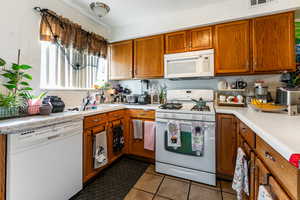 Kitchen with white appliances, brown cabinets, light countertops, and dark tile patterned floors