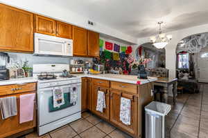 Kitchen featuring white appliances, brown cabinetry, a peninsula, light countertops, and decorative light fixtures