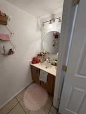Bathroom with a textured wall, light tile patterned floors, vanity, and a textured ceiling