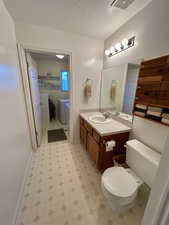 Bathroom with a textured ceiling, vanity, light flooring, and washing machine and clothes dryer