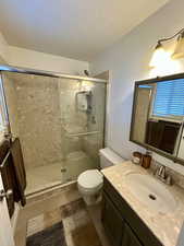 Full bathroom with vanity, light tile patterned flooring, a textured ceiling, a stall shower, and healthy amount of natural light